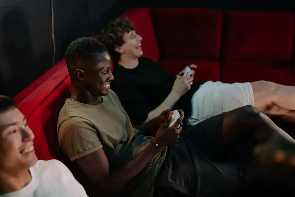Four friends laughing while holding controllers on a sofa